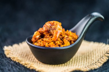 Baharatlı çıtır karides, siyah kaşıkta acı biber ezmesi, çuval bezi ve koyu arkaplan.