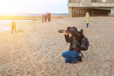 Baharda kumsalda fotoğraf makinesi ve sırt çantasıyla gezen gezgin, hala soğuktayken fotoğraf çeker.