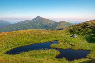 Hoverla dağının arka planına bir turist çadırı kurulduğu bir dağ gölü. Dağ manzarası.