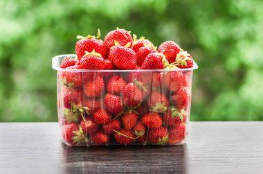 Taze, kırmızı organik çilekler. Plastik bir kutunun içinde. Yeşil doğal bir arka plan üzerine yakın plan.