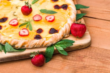 Çilekli meyveli pizza, kiraz, krema, jöle, ananas, kivi ve nane yaprakları, ahşap bir kesim tahtasının üzerinde, ev yapımı. tatlı arkaplanı, yakın plan