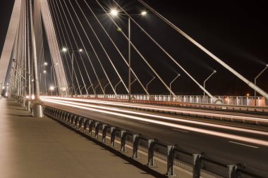 Kablolu köprüden geçen büyük çelik kablolarla, gece vakti parlak ışıklarla yakın çekim yapan bir otoyol.