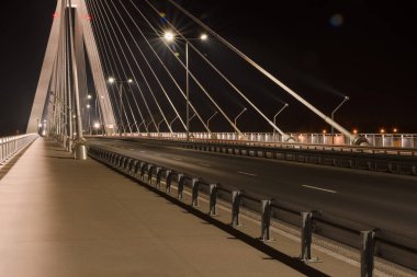 Büyük çelik kablolarla kablo destekli bir köprüden geçen otoyol, geceleri yakın plan.