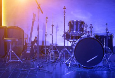 Davul takımı ve gitar mavi ışıkta Müzikal bir sahnede yakın planda duruyor