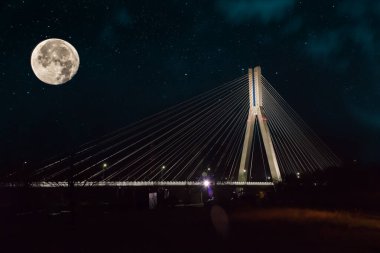 Geceleri kablo destekli köprü yıldızlı gökyüzünün, ayın ve bulutların arka planına karşı.