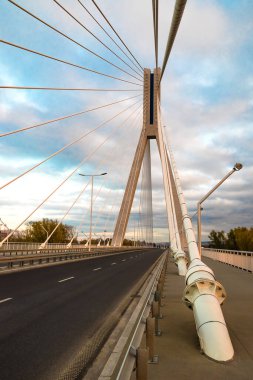 Büyük çelik kablolarla kablo destekli bir köprüden geçen otoyol, akşam üzeri yakın çekim sırasında mavi gökyüzü ve bulutların arka planına karşı.