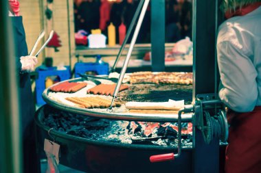 Mutfakta yemek pişirirken büyük bir ızgaranın üzerinde duran sosisler.
