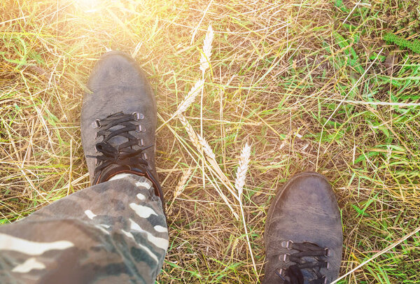 feet of a man in dirty shoes and camouflaged protective pants in field grass