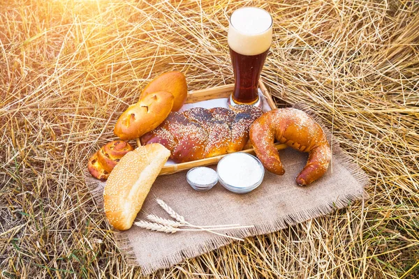 Glass of beer or kvass and breads with wheat ears on tablecloth, located on a dried hay. Fresh bread, bakery products and beer. Fresh beer