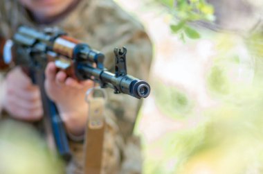 Kalaşnikov otomatik makineli tüfekle askerin eline geçti. Erkek eller Kalaşnikof saldırı tüfeğini tutuyor. Avtomatik tüfekle yakın çekim. Askeri asker sana tüfek doğrulttu..