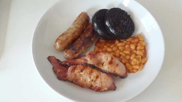 Plate of hot cumberland sausages, back bacon black pudding and baked beans — Stock Video