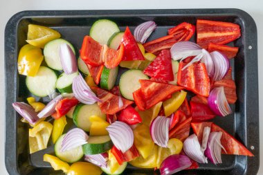 Prepared raw peppers, onions and courgettes on a roasting tray