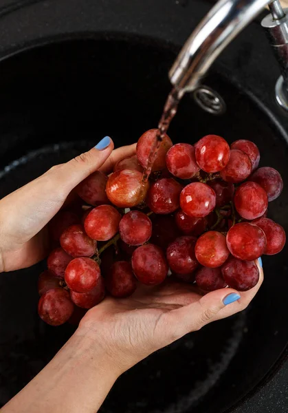 The girl washes a bunch of red grapes in her hands — Stock Photo, Image