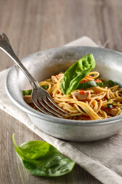 Spaghetti pasta in tomato sauce with chicken, basil in metal plate. Chicken spaghetti pasta over wooden background with copy space, italian food.