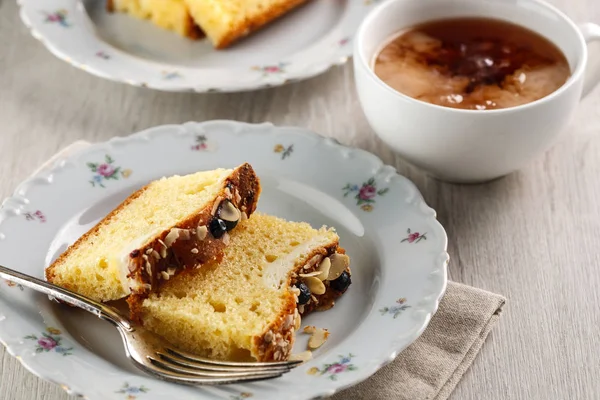 Sliced cake with almonds and blueberries on a white ceramic plate with a Cup of tea — Stock Photo, Image