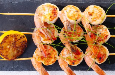 Şişte ızgara karides. Baharatlı, otlu ve limonlu ızgara deniz ürünleri. Lezzetli karides. Siyah taş plaka.