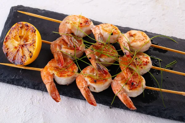 Grilled shrimp on skewers. Grilled seafood on skewers with spices, herbs and lemon. delicious prawn. Black stone plate — Stock Photo, Image