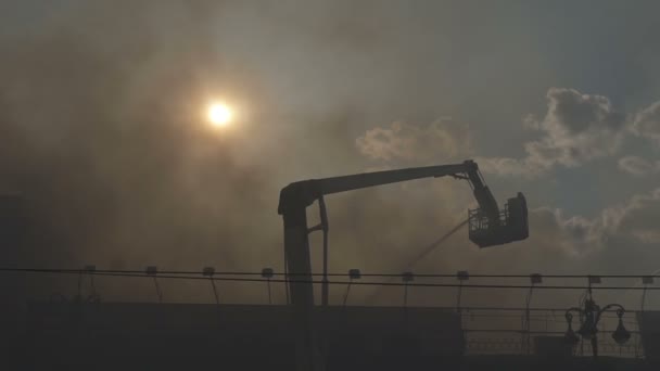 Bombeiros extinguem um incêndio no prédio. O sol é visível através das nuvens de fumaça negra — Vídeo de Stock