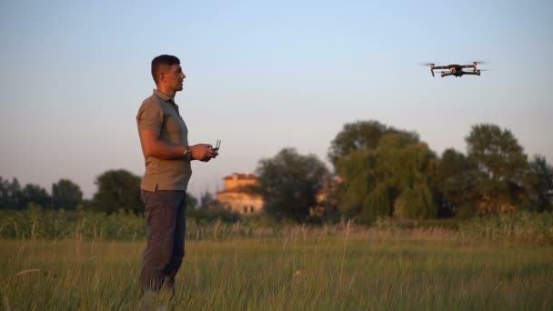 Чоловік контролює безпілотник на лузі на заході сонця влітку — стокове відео