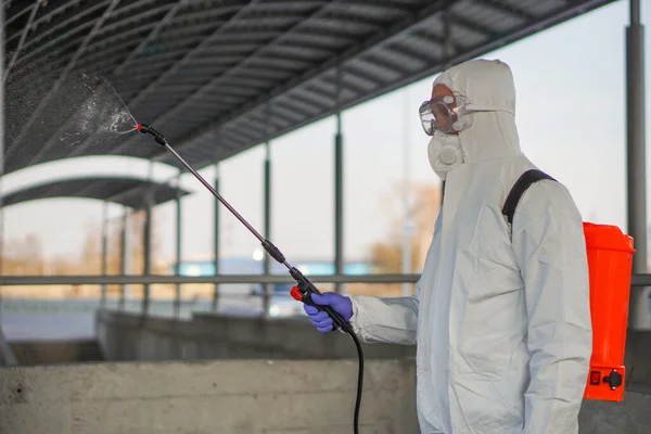 防護具を着た男が街中の噴霧器で消毒する コロナウイルスCovid 19疾患による表面処理 白いスーツの男がスプレー銃で通りを消毒します ウイルスのパンデミック ロイヤリティフリーのストック画像