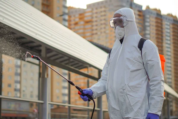 防護具を着た男が街中の噴霧器で消毒する コロナウイルスCovid 19疾患による表面処理 白いスーツの男がスプレー銃で通りを消毒します ウイルスのパンデミック ストック画像