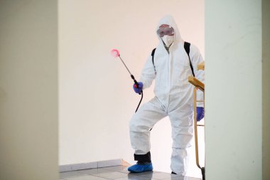 Koruyucu ekipman kullanan bir adam binada spreyle dezenfekte ediyor. Coronavirus covid-19 hastalığından dolayı yüzey tedavisi. Beyaz takım elbiseli bir adam evi sprey silahla dezenfekte ediyor. Virüs salgını