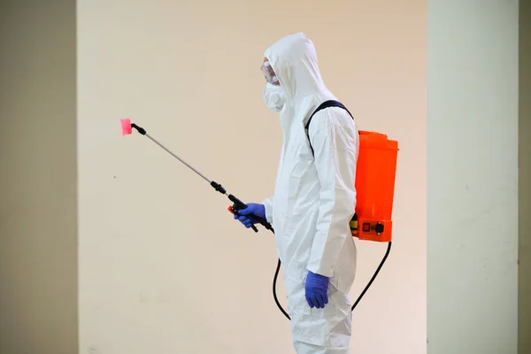 Koruyucu ekipman kullanan bir adam binada spreyle dezenfekte ediyor. Coronavirus covid-19 hastalığından dolayı yüzey tedavisi. Beyaz takım elbiseli bir adam evi sprey silahla dezenfekte ediyor. Virüs salgını