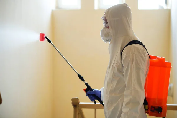 Koruyucu ekipman kullanan bir adam binada spreyle dezenfekte ediyor. Coronavirus covid-19 hastalığından dolayı yüzey tedavisi. Beyaz takım elbiseli bir adam evi sprey silahla dezenfekte ediyor. Virüs salgını