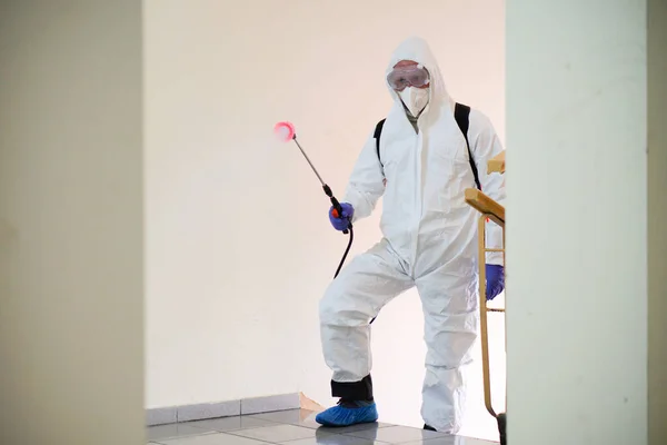 防護具を着た男が建物の中でスプレーで消毒します コロナウイルスCovid 19疾患による表面処理 白いスーツの男がスプレー銃で家を消毒します ウイルスのパンデミック ロイヤリティフリーのストック写真