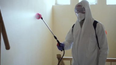 Koruyucu ekipman kullanan bir adam binada spreyle dezenfekte ediyor. Coronavirus covid-19 hastalığından dolayı yüzey tedavisi. Beyaz takım elbiseli bir adam evi sprey silahla dezenfekte ediyor. Virüs salgını
