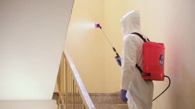 Koruyucu ekipman kullanan bir adam binada spreyle dezenfekte ediyor. Coronavirus covid-19 hastalığından dolayı yüzey tedavisi. Beyaz takım elbiseli bir adam evi sprey silahla dezenfekte ediyor. Virüs salgını