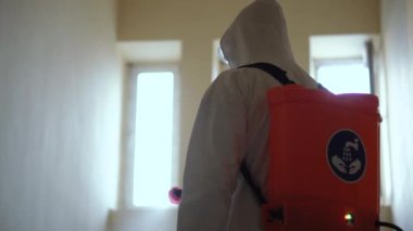 Koruyucu ekipman kullanan bir adam binada spreyle dezenfekte ediyor. Coronavirus covid-19 hastalığından dolayı yüzey tedavisi. Beyaz takım elbiseli bir adam evi sprey silahla dezenfekte ediyor. Virüs salgını