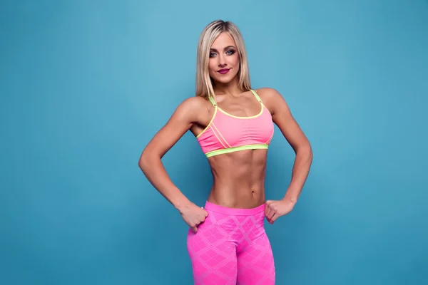 Portrait of slim sporty Blonde bodybuilder. VERY HOT woman standing against blue background. Copy space. Flat stomach press. — Stock Photo, Image