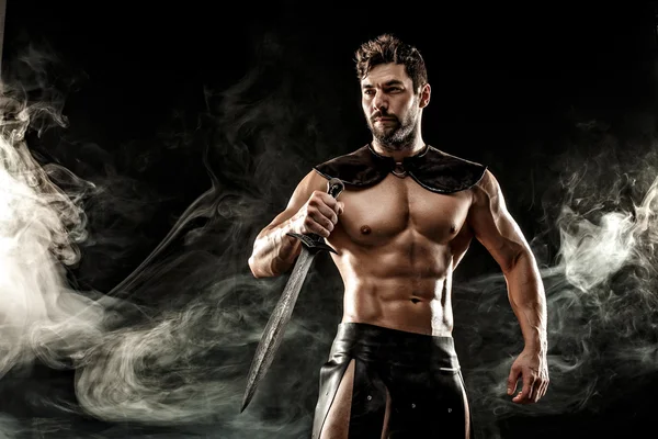 Severe barbarian in leather costume with sword in smoke — Stock Photo, Image