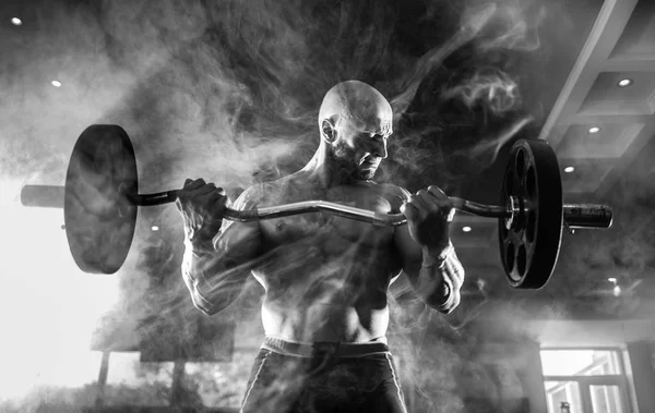 Młody przystojny kulturysta kaukaski sportowca pracy z sztangą w siłowni, robi biceps trening, dym — Zdjęcie stockowe