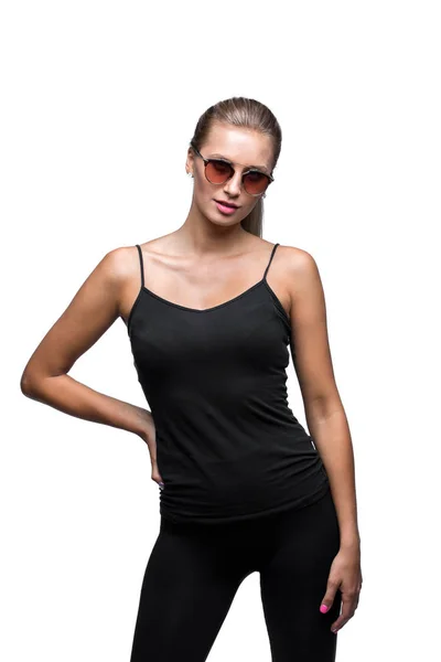 Portret van de jonge seksuele sportieve blonde dragen van een zonnebril. Geïsoleerd op wit. Zwart shirt, strakke leggins. — Stockfoto