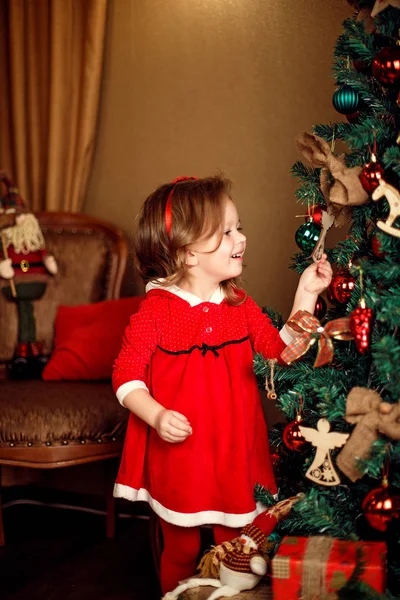 Standing girl puts decorations to a Christmas tree. Vertical indoors shot. — Stock Photo, Image