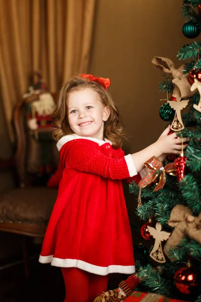 Standing girl puts decorations to a Christmas tree. Vertical indoors shot. — Stock Photo, Image