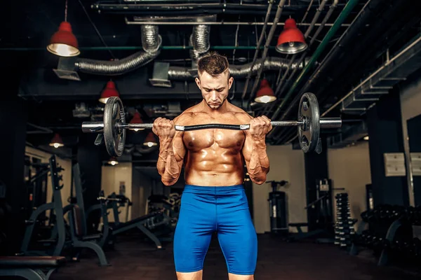 Joven apuesto culturista caucásico deportista haciendo ejercicio con una barra en el gimnasio, haciendo el entrenamiento de bíceps . — Foto de Stock