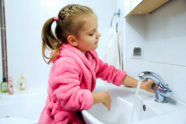 Sevimli küçük kız pembe bornoz ellerini yıkama içinde at kuyruğu ile yan görünüm. Boşaltmak