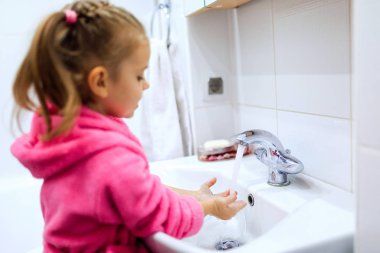 Sevimli küçük kız pembe bornoz ellerini yıkama içinde at kuyruğu ile yan görünüm. Boşaltmak