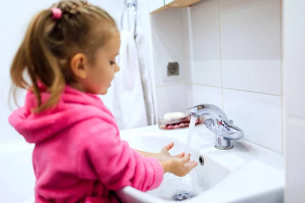 Side view of cute little girl with ponytail in pink bathrobe washing her hands. Copyspace — Stock Photo, Image