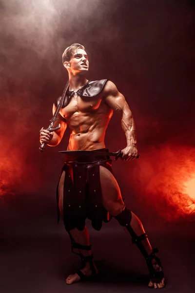 Full-length portrait of sexy young warrior holding sword and looking away while posing against fire. Copyspace — Stock Photo, Image