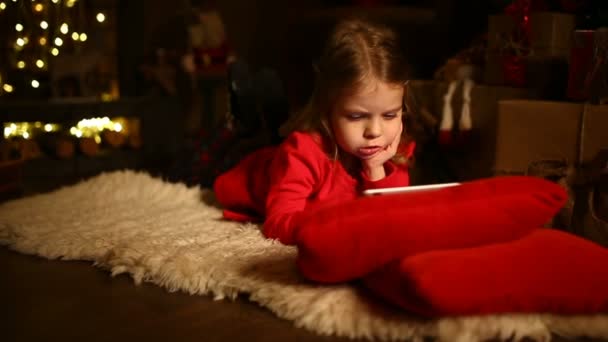 Little girl lying in carpet with presents around using tablet on — Stock Video