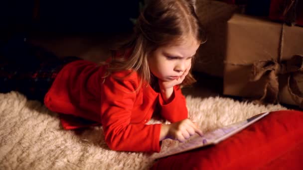 Little girl lying in carpet with presents around using tablet on — Stock Video
