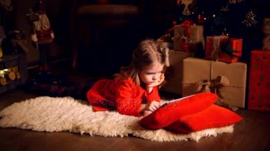 Küçük kız halı ile yatan tablet kullanarak etrafında sunar