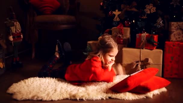 Liten flicka liggande i mattan med presenterar runt med tablett på — Stockvideo