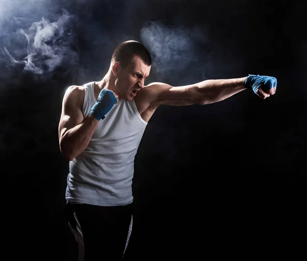 Muscular kickbox or muay thai fighter punching in smoke.