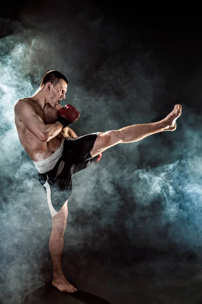 Muscular kickbox ou muay thai lutador perfurando na fumaça . — Fotografia de Stock
