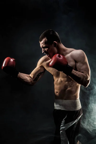 Muscular kickbox o muay thai luchador puñetazos en el humo . — Foto de Stock